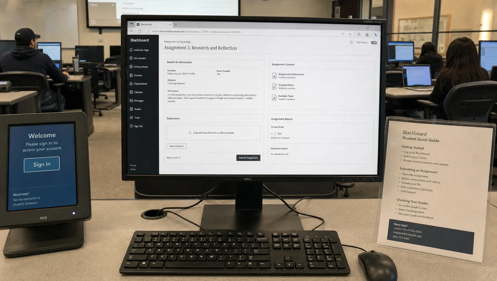 A campus computer lab shows a Blackboard assignment page on a monitor beside a printed help sheet.